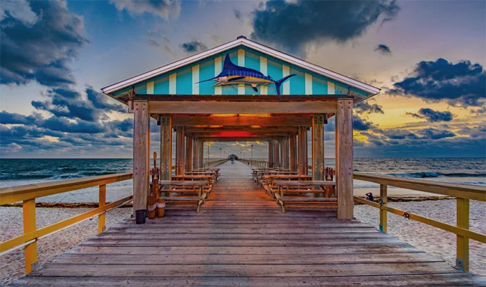 Wooden pier pavilion with benches at sunset over ocean water with dramatic cloudy sky