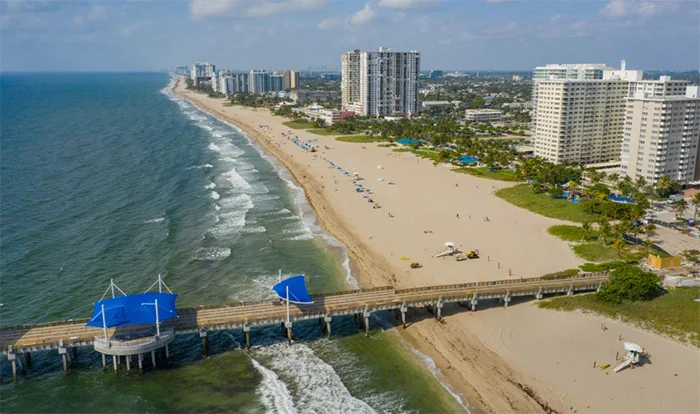 Aerial view of Deerfield Beach pier and coastline with high-rise buildings along sandy shore and blue ocean waters