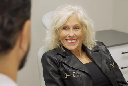 Smiling blonde woman in black leather jacket speaking with someone in professional setting