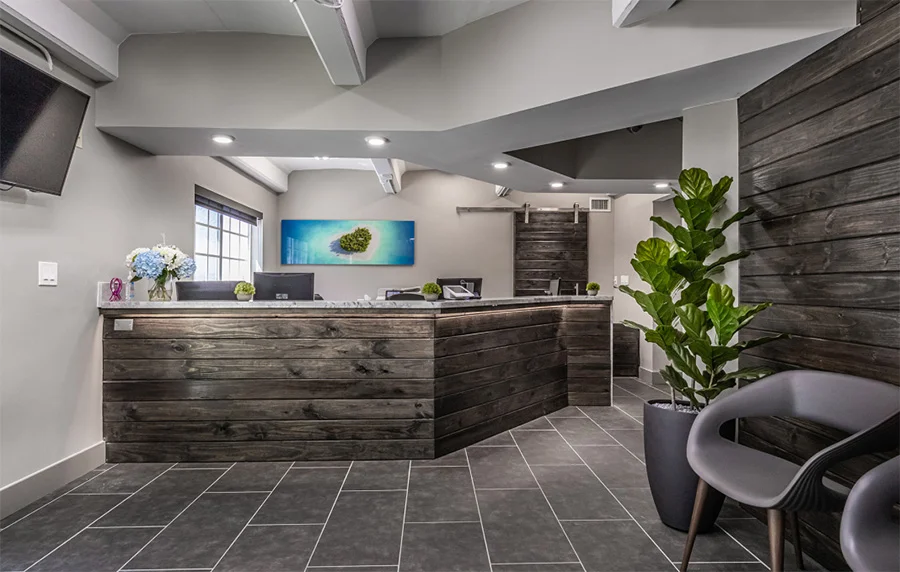 Modern medical office reception desk with gray wood finish, tiled floors, and contemporary furniture