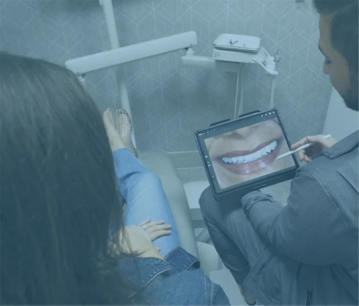 Dentist showing patient digital smile design on tablet during consultation in modern dental office