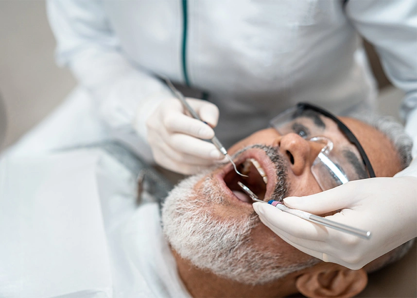 Dentist performing oral examination on male patient wearing protective eyewear in dental clinic