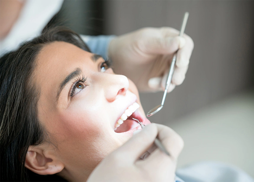 Woman receiving dental examination from dentist in clinic with open mouth and dental tools