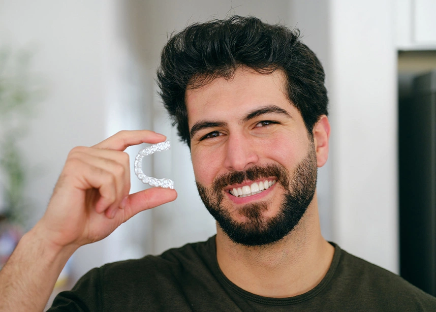 Man smiling and holding clear aligner or retainer case next to his face showing orthodontic dental treatment