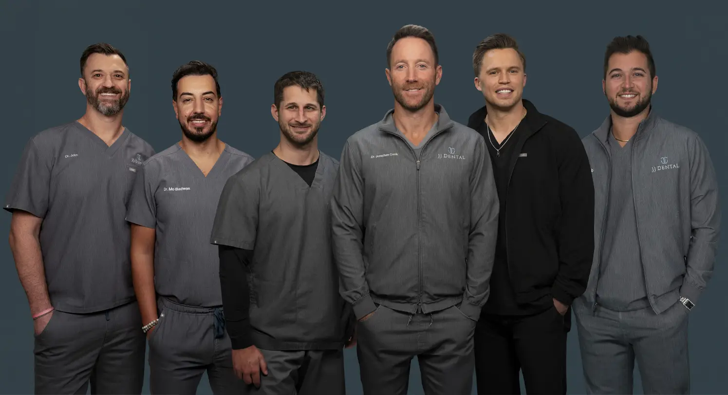 Six male dental professionals in gray uniforms standing together against dark background