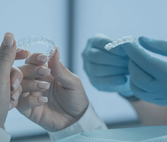 Person holding clear dental aligners with blurred hands examining orthodontic treatment in background
