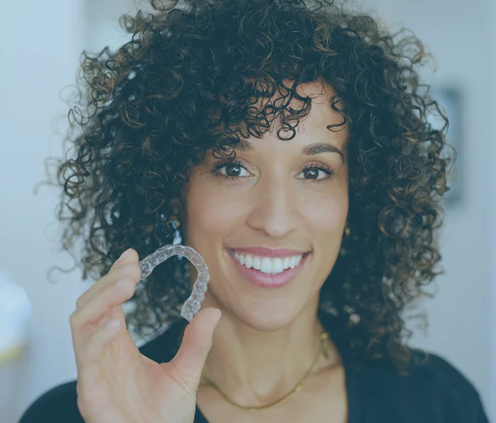 Woman with curly hair smiling while holding jade gua sha facial massage tool for skincare routine