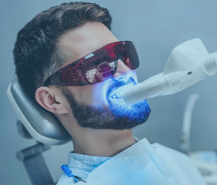 Man receiving professional teeth whitening treatment with LED light at dental clinic